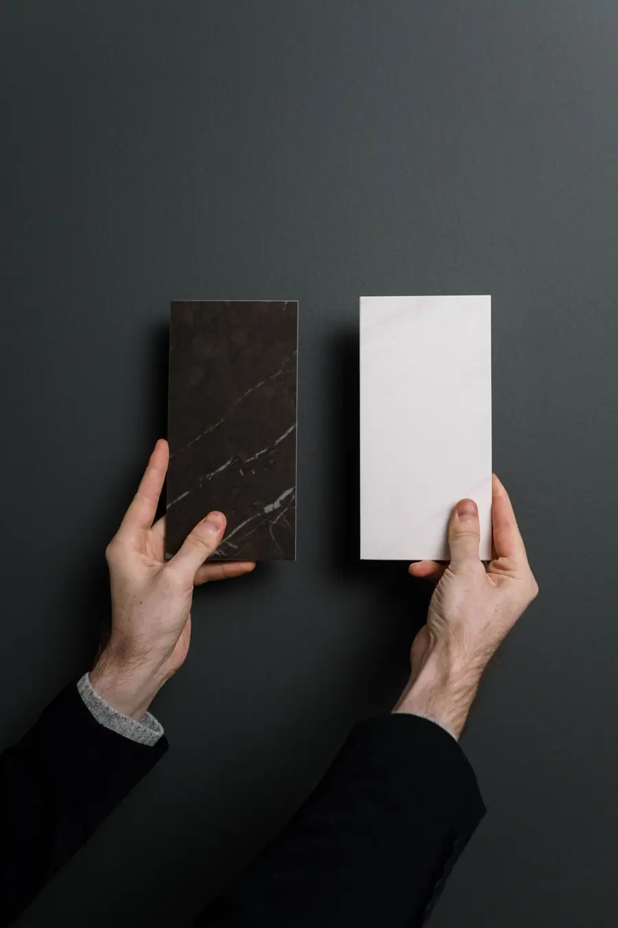 Hands holding a dark stone sample next to a white one