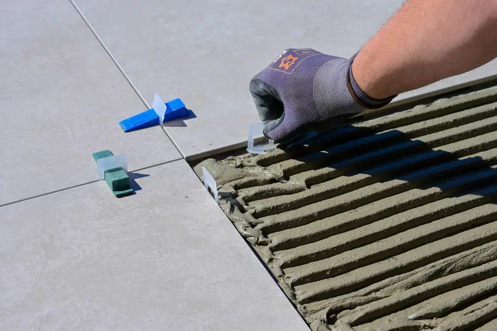 Gloved hand setting a large floor tile with levelers